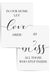 Set of two minimalist wall art prints with the phrases 'In Our Home Let Love Abide' and 'Bless All Those Who Step Inside' in black script and serif fonts, framed in white and styled on a light wood floor
