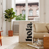 Modern living room with a 'hola' sign, plant, and sofa.