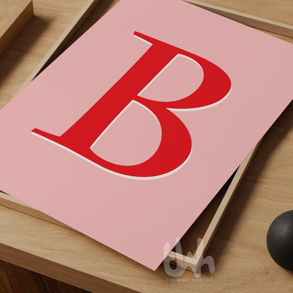 Custom monogram wall art print with a bold red letter 'B' on a pink background, displayed on a wooden tray – personalized alphabet print for home décor