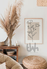Minimalist line art of blooming flowers with buds, drawn in black on a beige background, framed and styled in a boho living room with natural wood and pampas decor.