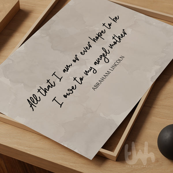 Minimalist wall art print featuring the quote “All that I am or ever hope to be, I owe to my angel mother” by Abraham Lincoln in black script and serif font on a soft beige watercolor background, placed on a wooden surface – perfect Mother's Day gift for mum.