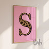 Framed artwork with a leopard print letter 'S' on a pink background, displayed on a wall.