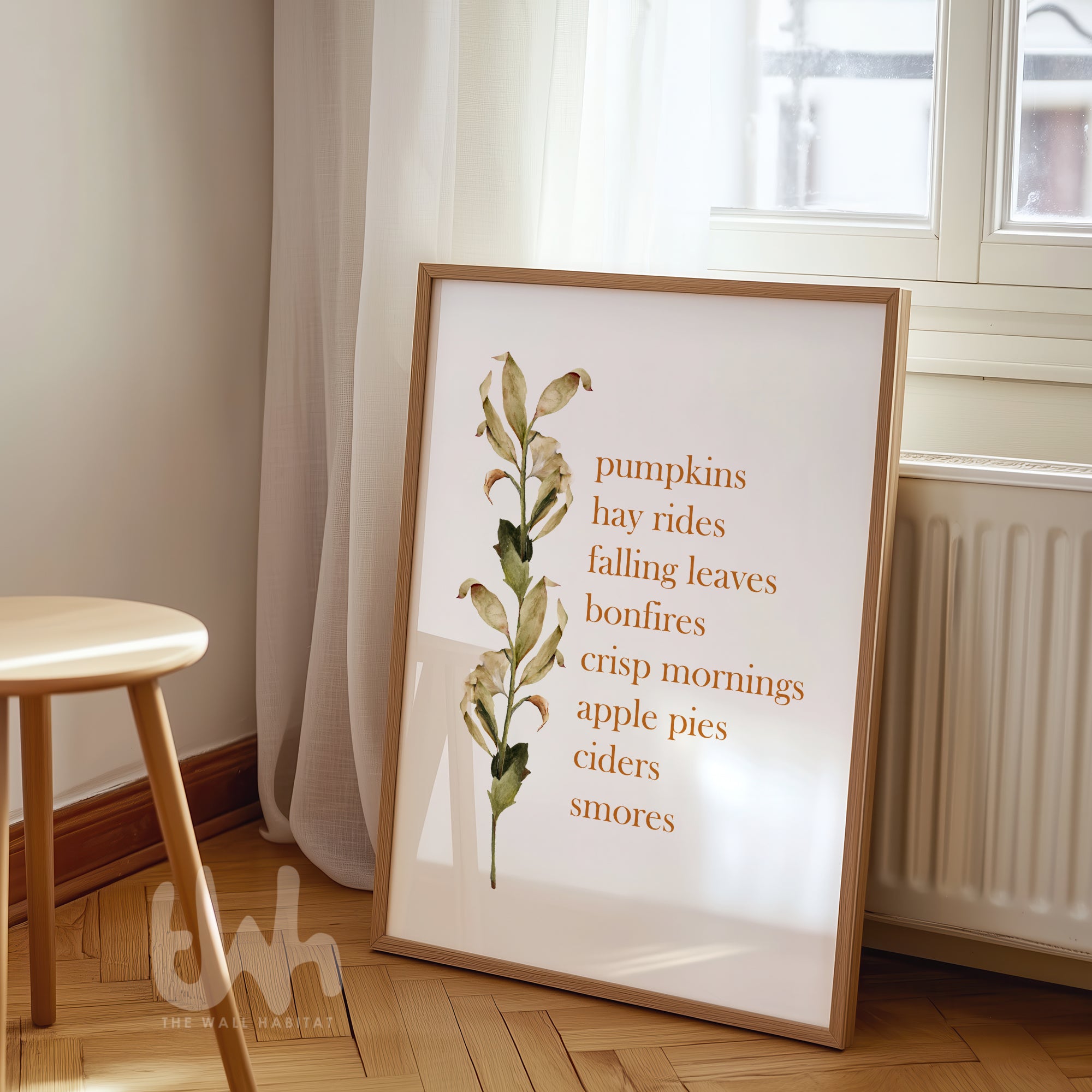 Fall-themed wall art print with a list of autumn favorites like “pumpkins, hay rides, crisp mornings” alongside a watercolor botanical stem, styled in a light wood frame.
