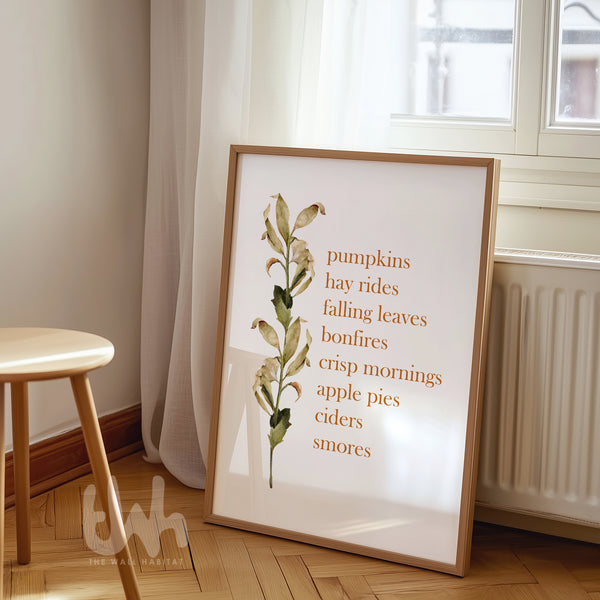 Fall-themed wall art print with a list of autumn favorites like “pumpkins, hay rides, crisp mornings” alongside a watercolor botanical stem, styled in a light wood frame.