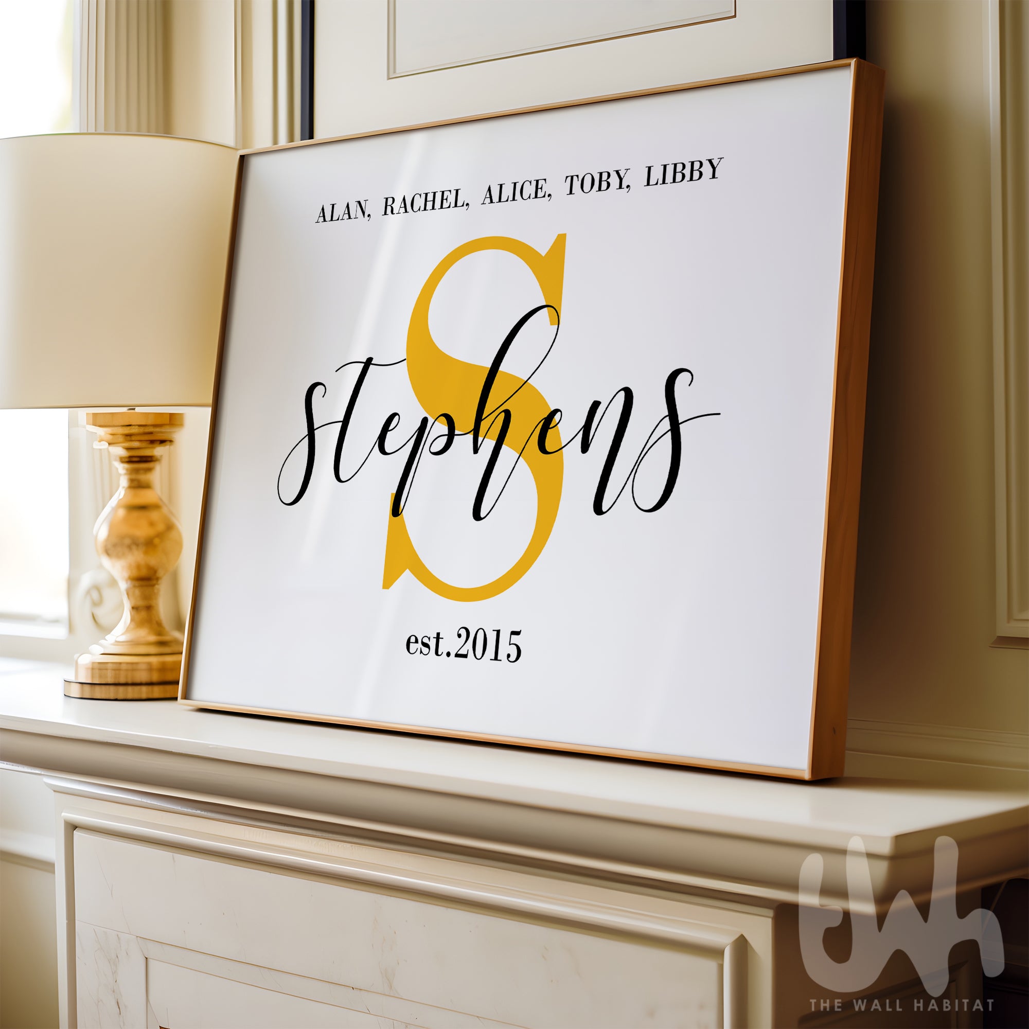 Framed family name wall art print featuring a large yellow monogram ‘S’, the surname Stephens, and first names with 'est. 2015', displayed on a mantel next to a lamp