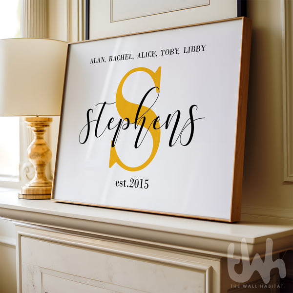 Framed family name wall art print featuring a large yellow monogram ‘S’, the surname Stephens, and first names with 'est. 2015', displayed on a mantel next to a lamp