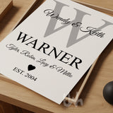 Flat-lay of a custom family monogram print with grey letter W and black personalized text for parents, children, and ‘EST. 2004’, styled on a wooden tray