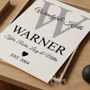 Flat-lay of a custom family monogram print with grey letter W and black personalized text for parents, children, and ‘EST. 2004’, styled on a wooden tray