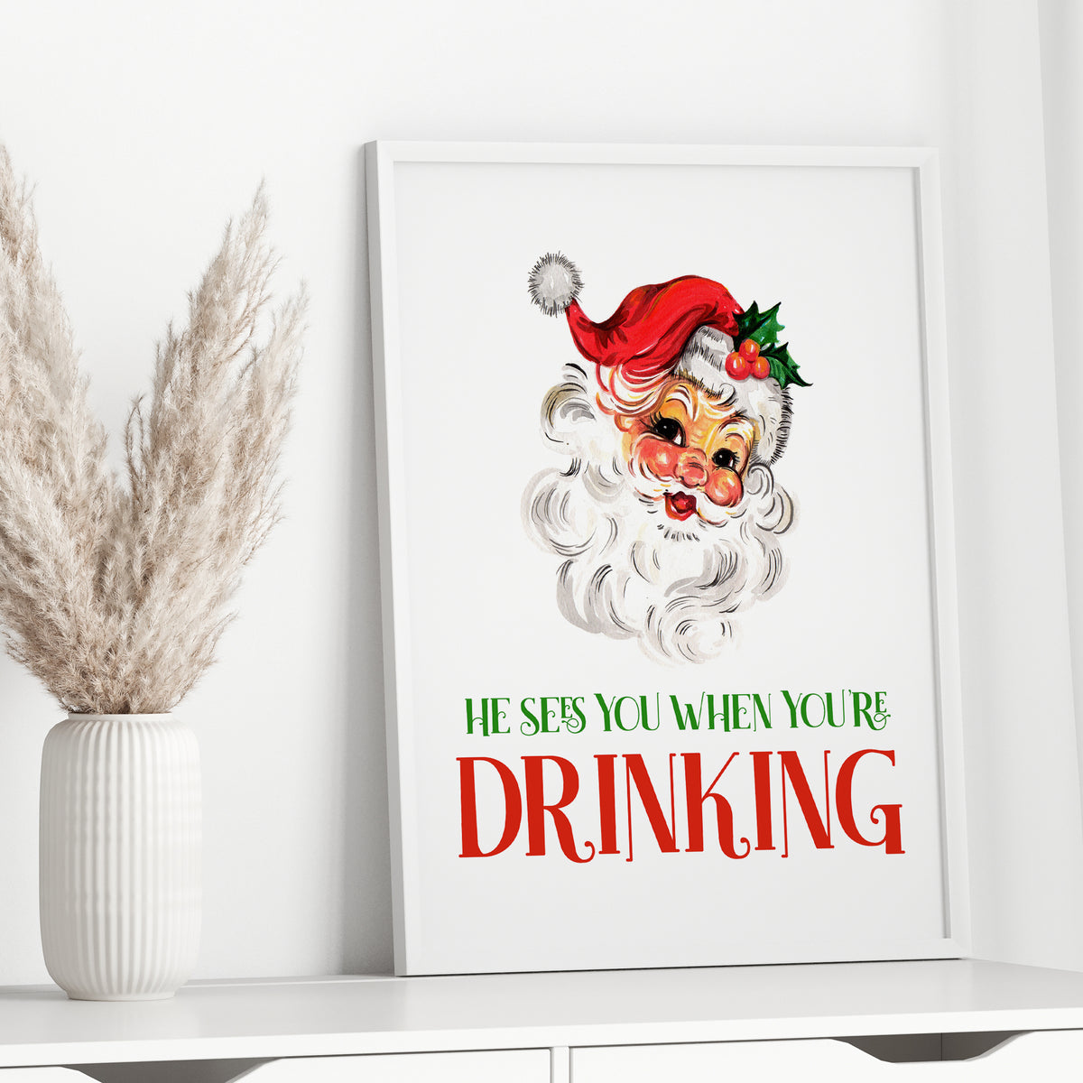 Vintage Santa Christmas drinking quote printable displayed in white frame beside neutral pampas grass
