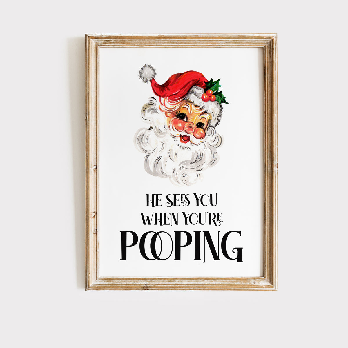 Funny Santa Christmas toilet wall art displayed in a natural oak frame with festive greenery and silver decorations