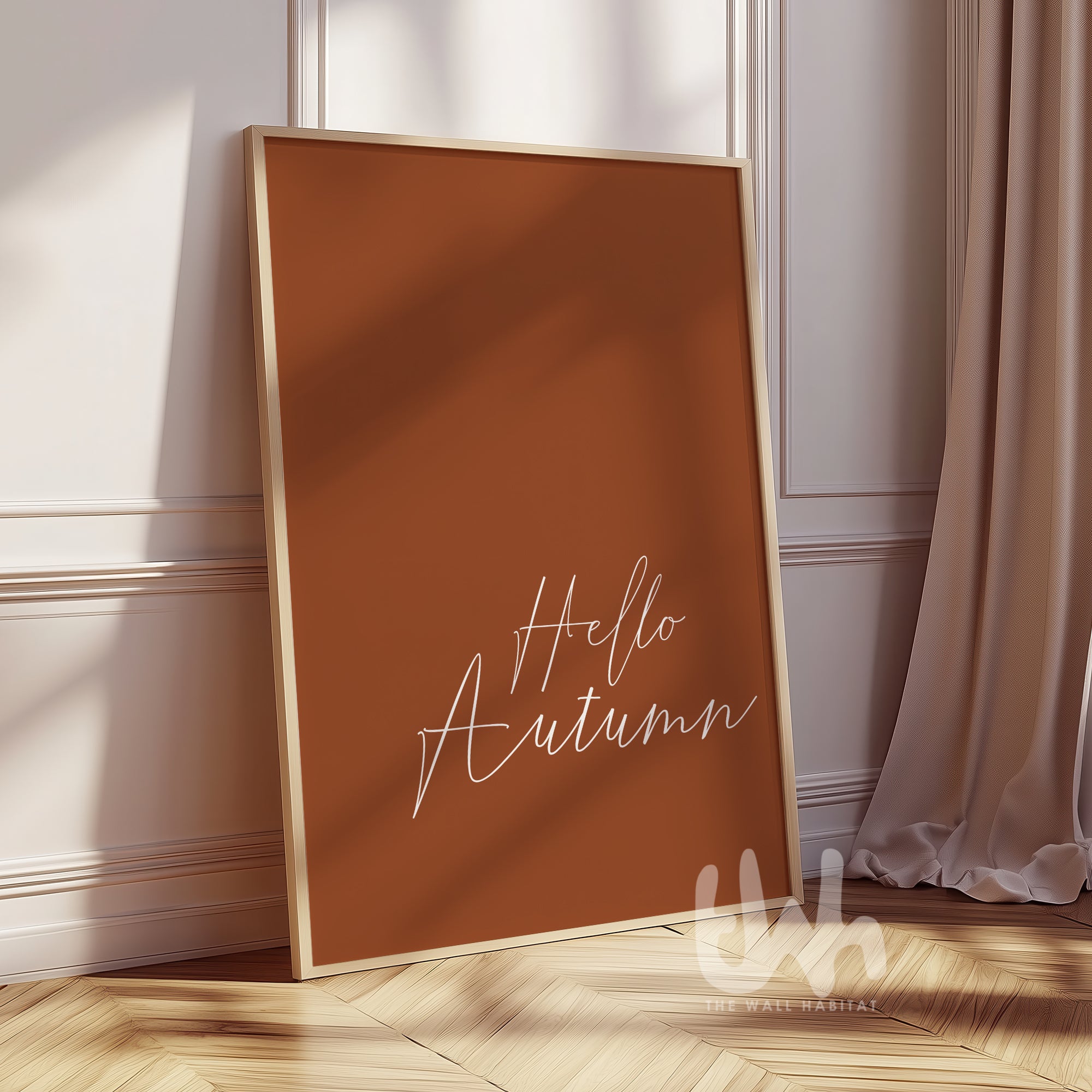 Minimalist burnt orange wall art print with white handwritten script reading “Hello Autumn,” displayed in a wood frame on a fall-styled wall.