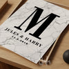 Marble wall art print with a bold black letter 'M', the names 'Jules & Harry', and the date '14.2.2018' printed below, styled on a wooden tray
