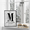 Framed marble personalized couple’s monogram wall print with the letter M, names Jules & Harry, and wedding date, displayed on a windowsill in a winter setting