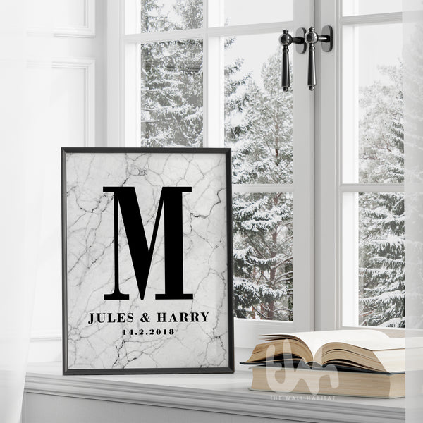Framed marble personalized couple’s monogram wall print with the letter M, names Jules & Harry, and wedding date, displayed on a windowsill in a winter setting