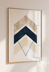 Modern abstract chevron wall art with layered navy blue, beige, and cream arrow shapes and triangle outlines, styled in a gold frame on a neutral wall.