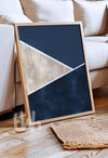 Framed abstract art piece on a wooden floor with a beige sofa in the background