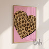 Framed artwork with a leopard print heart on a pink background, displayed on a wall.