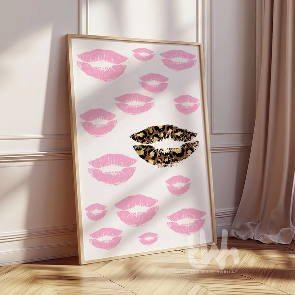 Framed artwork with pink lips and a leopard print lip on a white background, leaning against a wall.