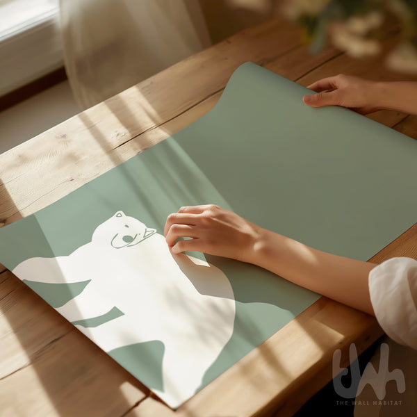 Close-up of a hand unrolling a sage green minimalist polar bear nursery print on a wooden table