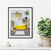 Framed yellow bathtub wall art featuring houseplants and patterned flooring, displayed above a white cabinet in a modern home