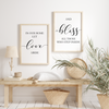 Set of two minimalist wall art prints with the phrases 'In Our Home Let Love Abide' and 'Bless All Those Who Step Inside' in black script and serif fonts, framed in white and styled on a light wood floor