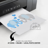 A close-up of a printer releasing a printed card featuring cartoon baby elephants in blue and gray with blue hearts. Text below advertises print locations: 'WHERE YOU CAN PRINT: AT HOME or ONLINE or LOCAL PHOTO CENTER'.