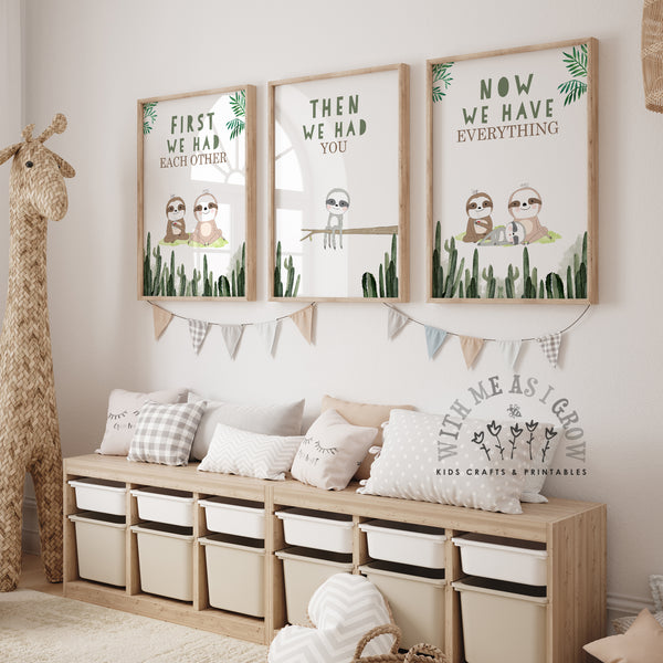 Three framed nursery wall art prints featuring sloth illustrations and phrases ('FIRST WE HAD EACH OTHER', 'THEN WE HAD YOU', 'NOW WE HAVE EACH OTHER') displayed above a wooden storage bench with pillows in a styled nursery room.