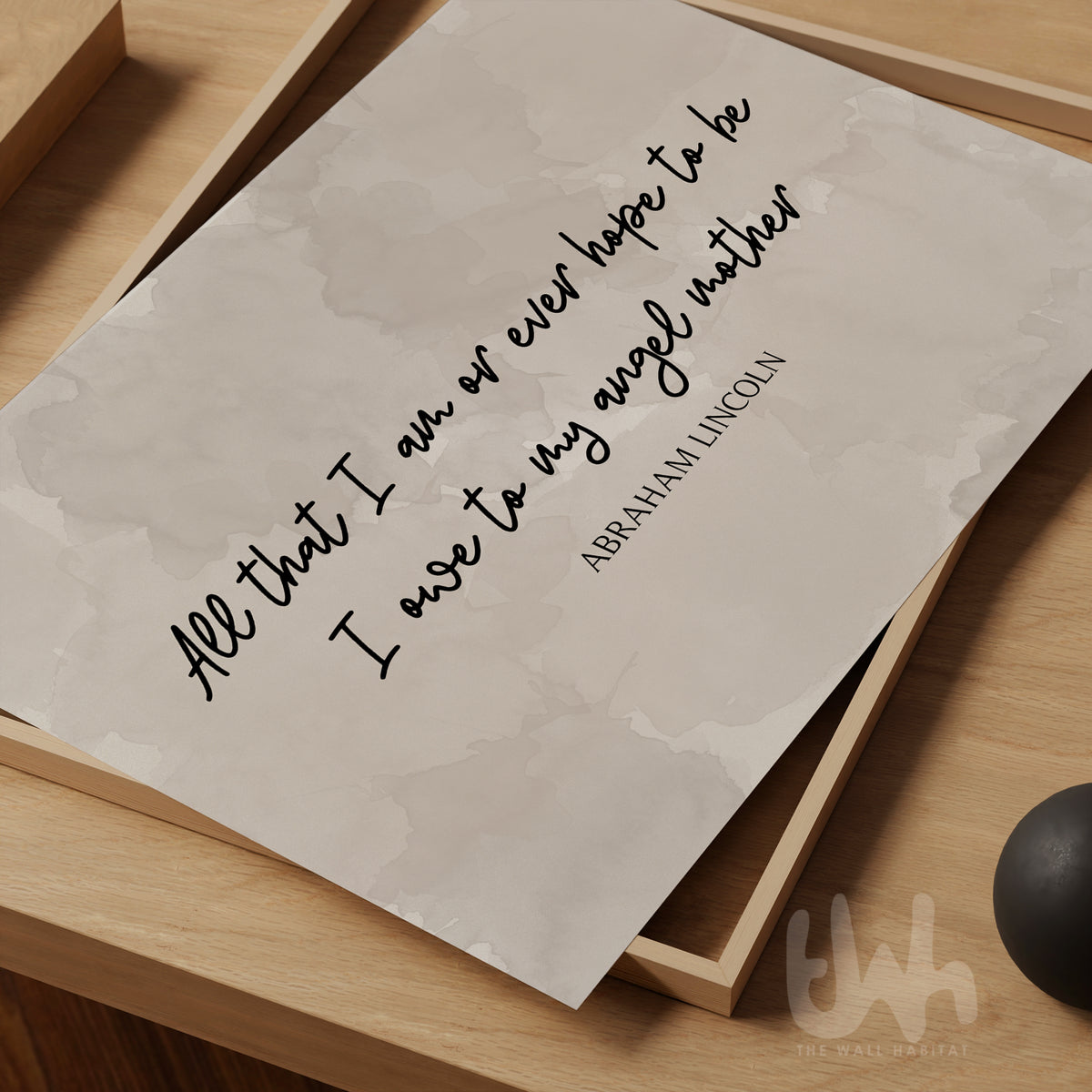 Minimalist wall art print featuring the quote “All that I am or ever hope to be, I owe to my angel mother” by Abraham Lincoln in black script and serif font on a soft beige watercolor background, placed on a wooden surface – perfect Mother's Day gift for mum.