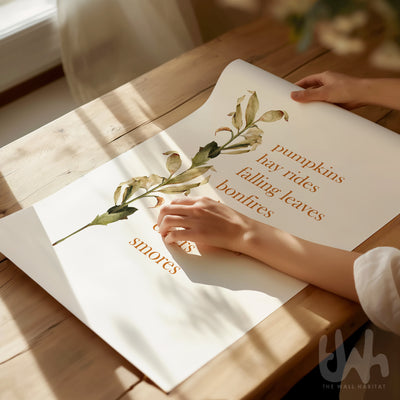 Person holding an autumn-themed print on a wooden table.