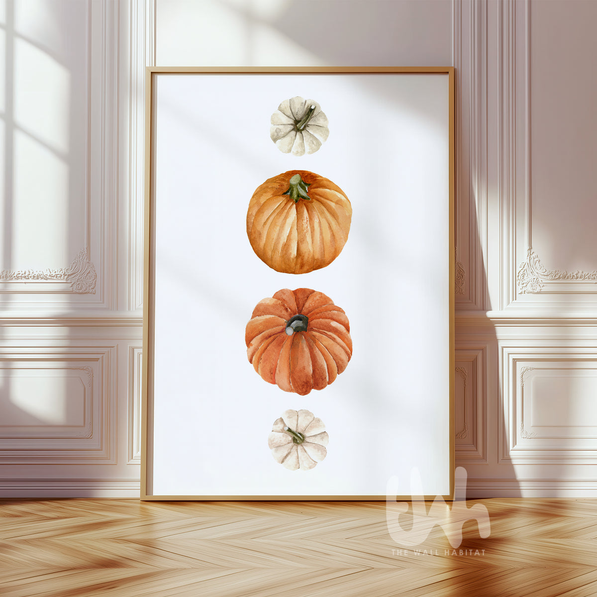 Watercolor wall art print featuring a vertical stack of heirloom pumpkins in orange, cream, and terracotta, displayed in a gold frame in a classic autumn-themed interior.