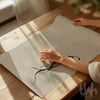 Hands unrolling a minimalist black bow print on a soft beige background, styled on a wooden table in warm natural light