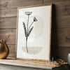 Framed beige and black plant illustration print resting on a wood shelf in a rustic-modern room"
