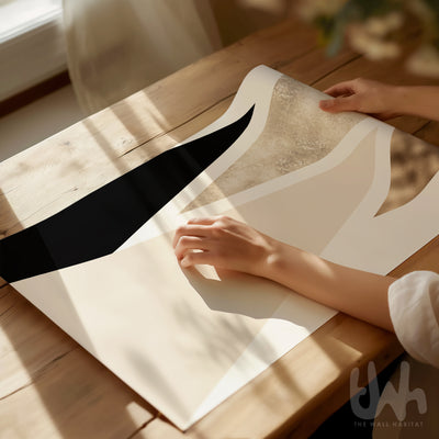 Person holding a piece of geometric wall art with a black stripe on a wooden table