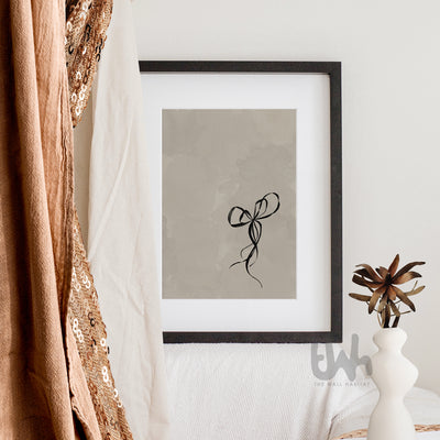 Framed black bow line drawing print resting on a wood mantel in a rustic-modern setting with warm tones