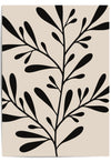 Modern botanical wall art print with bold black leaf silhouettes over a beige background, shown unframed and styled on a wooden desk in natural light