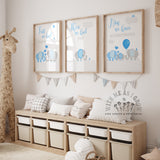 Three framed nursery art prints with blue elephant illustrations and inspirational quotes are displayed on a wall above a wooden storage bench with pillows in a styled nursery room.