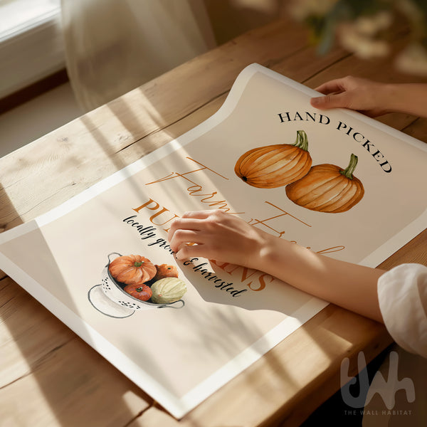 Person holding a decorative fall-themed wall art with pumpkins on a wooden table.