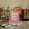 Living room with a 'Good Vibes Only' poster, books, and a bottle on a wooden floor.