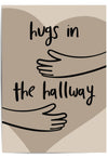 Neutral-toned wall art print leaning against a wooden door in a cozy hallway, featuring minimalist line art of arms and the phrase 'Hugs in the Hallway' over a heart shape