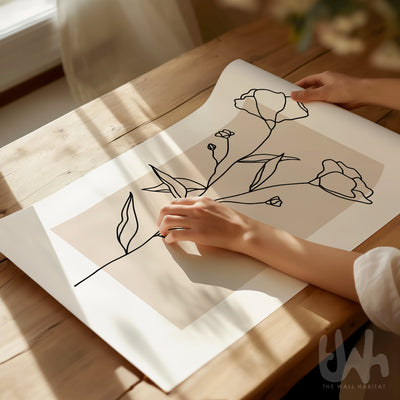 Person holding a sheet of paper with floral line drawing on a wooden table