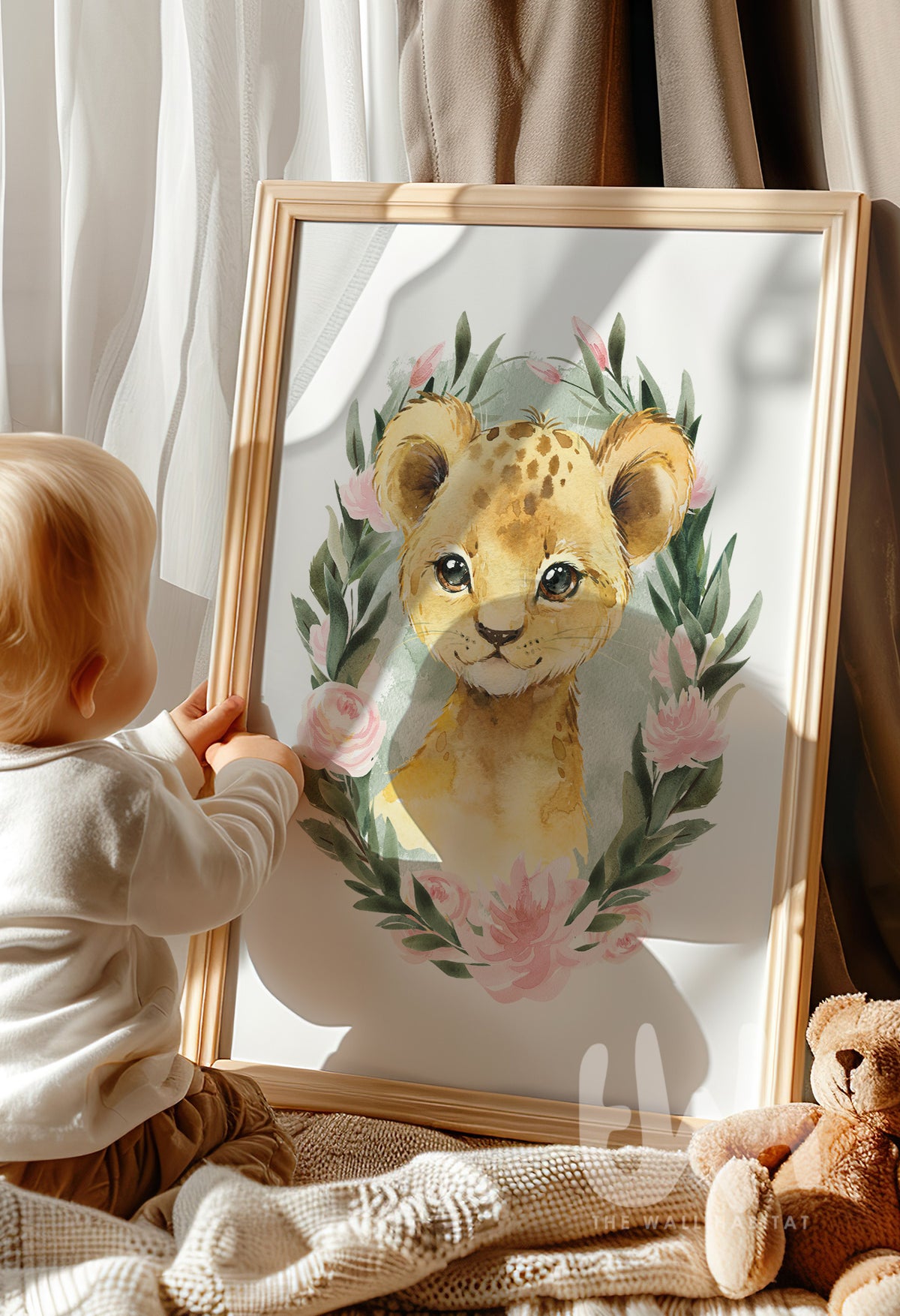 Toddler sitting by the window looking at a framed lion cub nursery print with sage green background and pink flowers – baby room safari décor