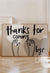 Neutral wall art print with black hand-lettered text reading 'Thanks for coming, bye' and waving hand illustrations over a taupe heart background